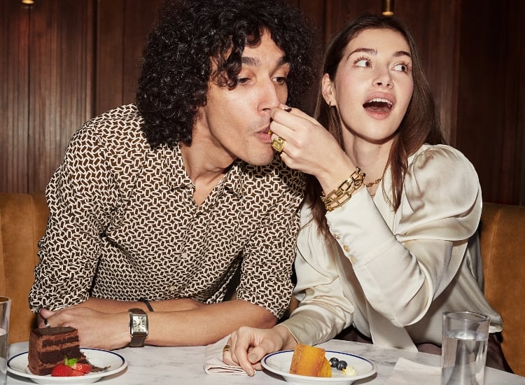 A woman feeding a man cake. They are both wearing a variety of Fossil watches and jewelry.