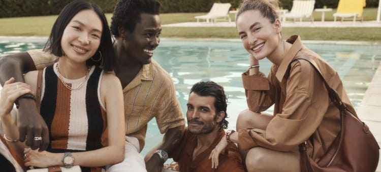 A group of four people smiling and sitting in front of a pool while wearing Fossil spring styles.