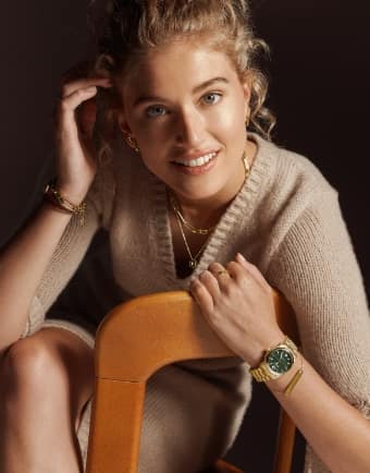 A woman smiling and wearing a gold-tone Fossil heritage watch with green dial. 