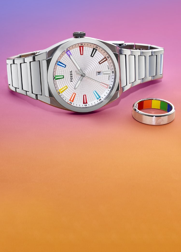 Eine silberfarbene Uhr und ein Ring mit Regenbogenfarben, die für die Pride- und Transgender-Flaggen stehen. Die Accessoires zeigen sich vor einem regenbogenfarbenen Hintergrund mit Farbverlauf von Violett über Rosa- zu Orangefarben.