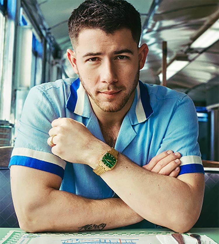 Nick Jonas sits in a diner booth wearing the gold-toned Machine Luxe watch with a green malachite dial.