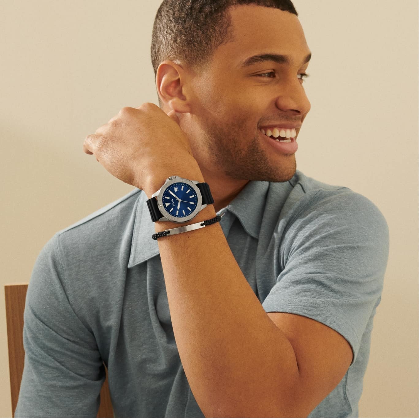 A man smiling as he looks over his shoulder. He’s wearing a light blue polo shirt, sporty watch with a dark blue dial and black leather bracelet with a silver detail.
