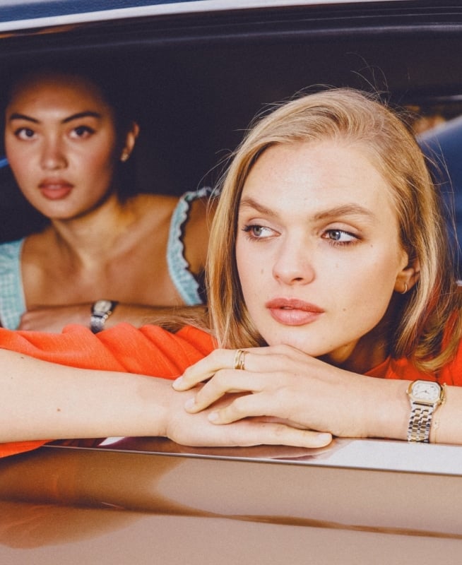 Four young adults, three women and one man, gaze out the window of a vintage car.