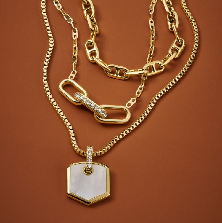 Layers of three gold-tone Fossil Heritage Jewelry necklaces, featuring mother-of-pearl accents and crystal embellishments.