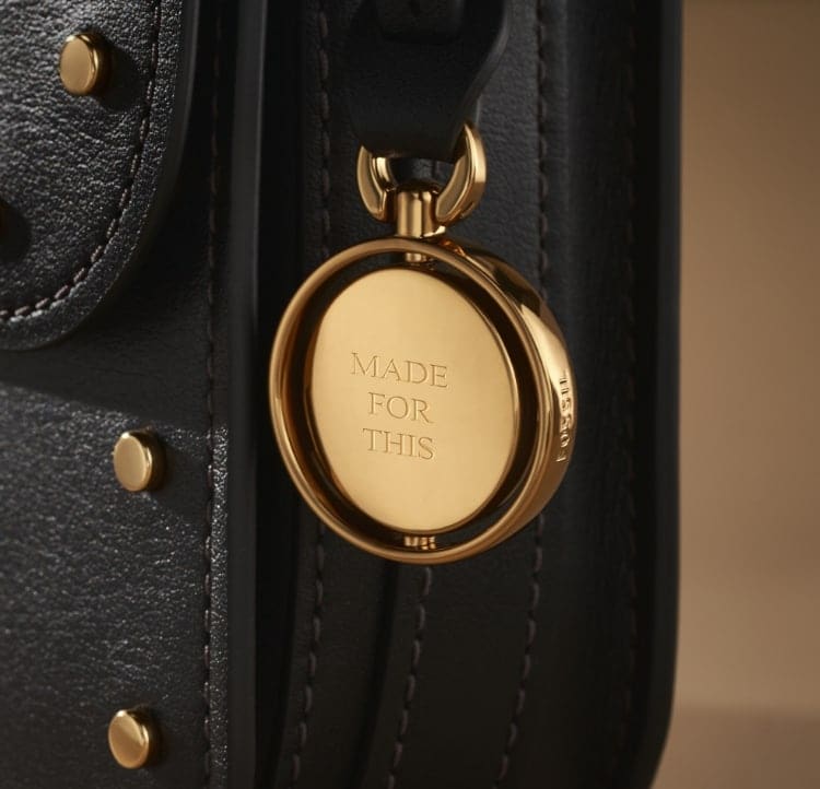 Il charm Legacy da incidere su una borsa in pelle marrone. Presenta l’incisione “Made For This”.