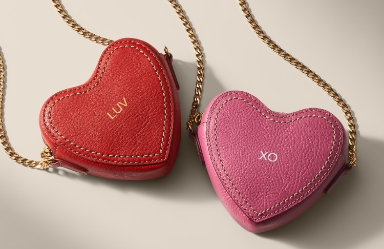 A red leather heart-shaped micro bag embossed with LUV and a pink leather heart-shaped micro bag embossed with XO.