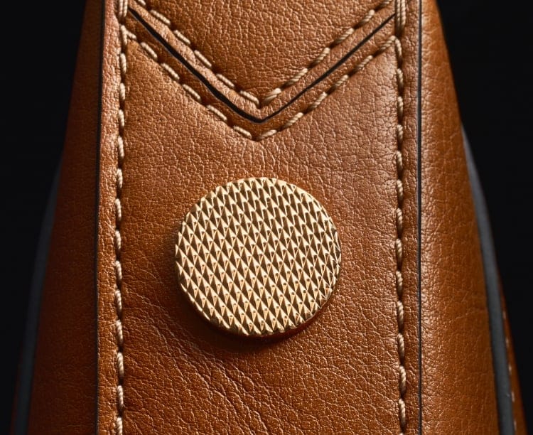 Two gold-tone knurled studs on a brown leather Harwell bag, overlayed with a sketch.