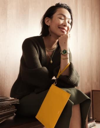 Un donna sorridente che tiene in mano un portafoglio con cinturino da polso in pelle gialla. 