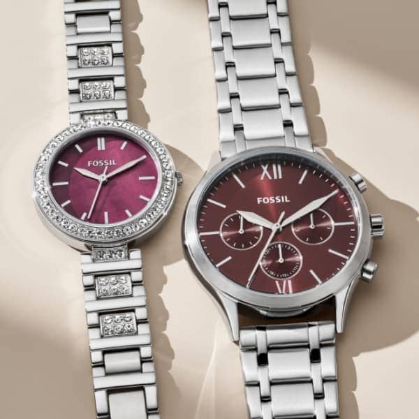 Un coffret cadeau avec une montre pour homme et une montre pour femme. Les deux modèles présentent un cadran bordeaux sur un boîtier en acier inoxydable.