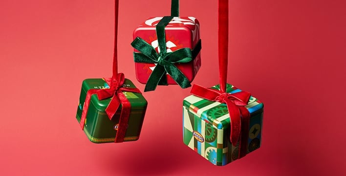 Red background with three Fossil tins handing down, wrapped as gifts.