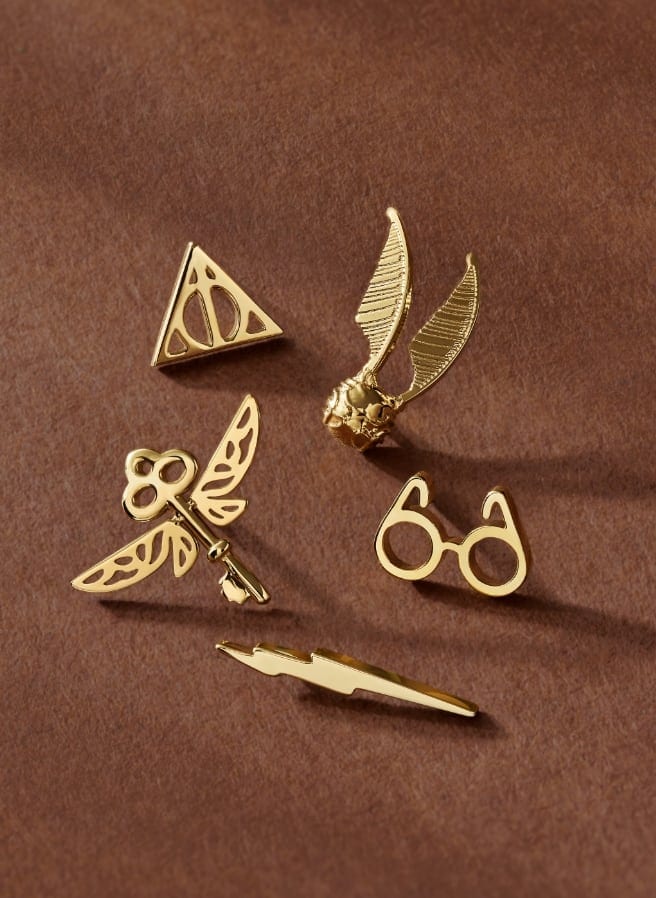 Cinq dormeuses de boucles d’oreilles ton or avec un éclair, une clé volante, les lunettes de Harry PotterMC, un snitch volant et un symbole Reliques de la mort.