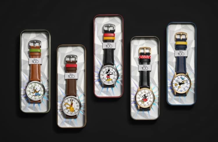 Una imagen GIF con latas coleccionables para cada uno de los cinco relojes con personajes para conmemorar la historia de Mickey y sus amigos. De izquierda a derecha: Goofy, Pluto, Mickey Mouse, Minnie Mouse y el Pato Donald. La segunda imagen muestra una imagen colectiva de los cinco relojes conmemorativos. Debajo aparece el logotipo D100, que celebra los 100 años de Disney, seguido del logotipo de Disney y Fossil.