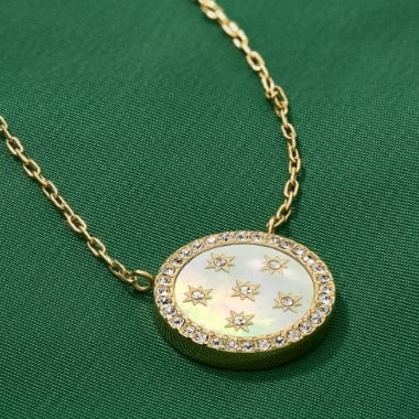 A mother-of-pearl pendant necklace on a gold-tone chain set against a green background.