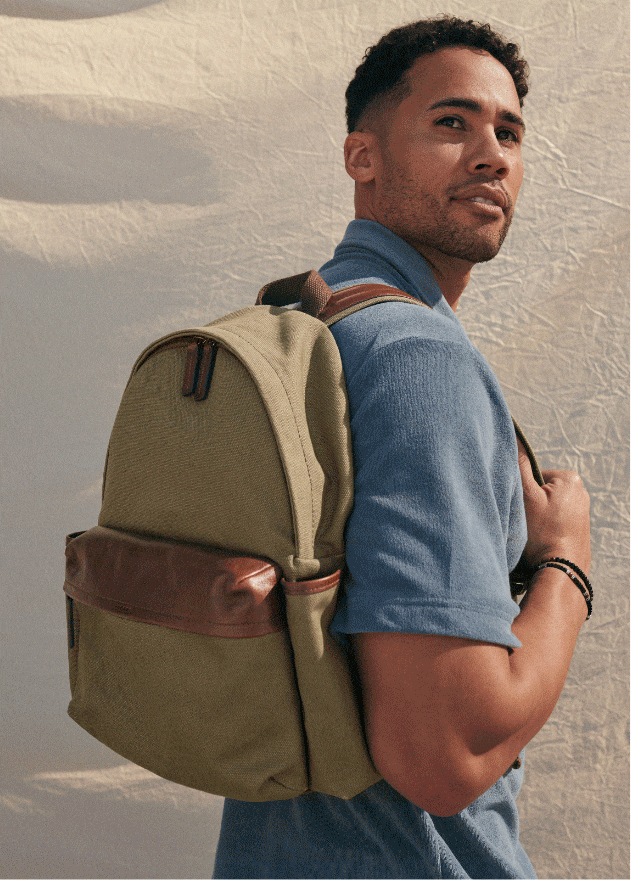 A man looking over his shoulder wearing a blue short-sleeve polo shirt and an olive green canvas backpack with brown trim.