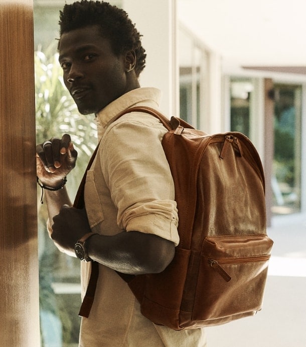A man wearing the brown leather Buckner backpack. Brown leather Buckner backpack.