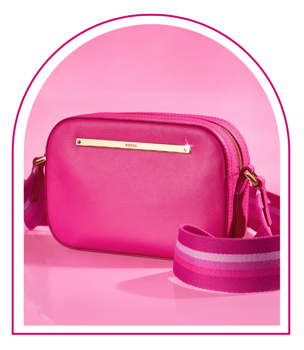 Ein pinker Hintergrund mit einem Fenster im Stil des Traumhauses von Barbie™. Im Fenster sieht man unsere Limited Edition Barbie™ x Fossil Kameratasche Liza aus glattem Leder im typischen Pink mit extrabreitem, sportlichem Riemen im 90er-Jahre-Stil mit pinken Streifen.