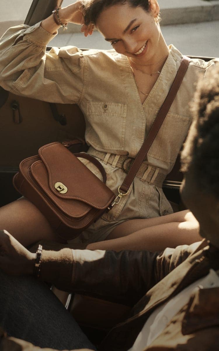 A woman sitting in a car with a brown leather Fossil Heritage handbag.