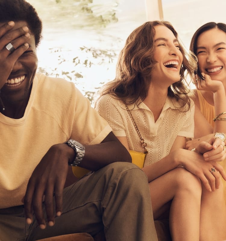 A man and two women wearing Fossil products are sitting together and laughing. 