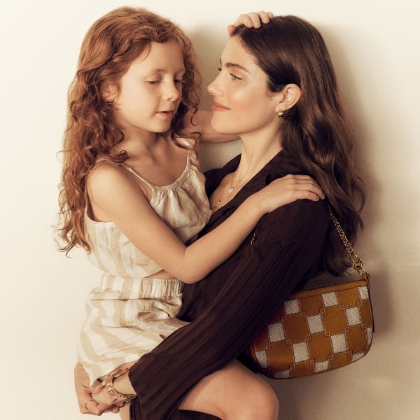 A woman wearing the patchwork Jolie baguette and carrying a small child.