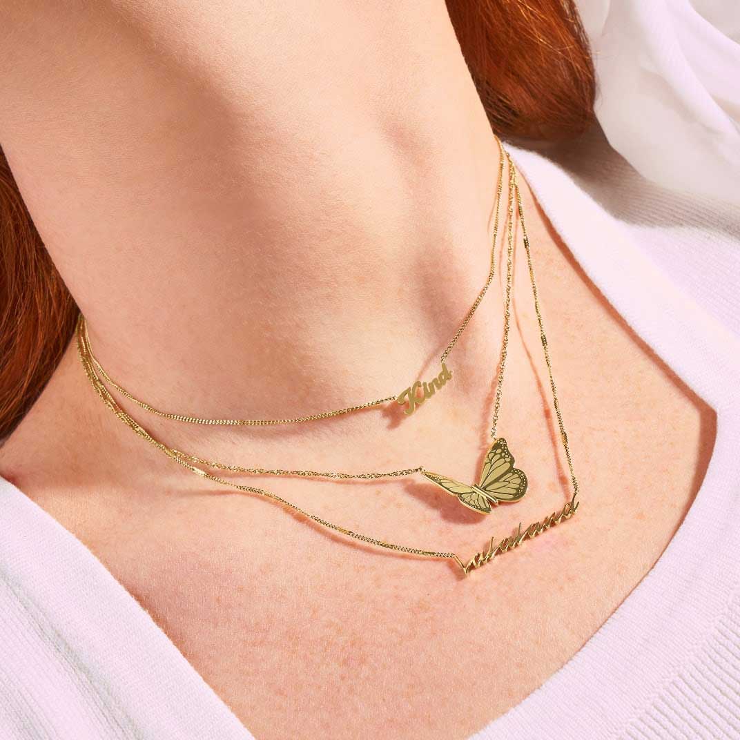 A woman wearing three gold-tone La La Land x Fossil necklaces, including one that reads Kind, one with a butterfly motif and one that reads LaLaLand.