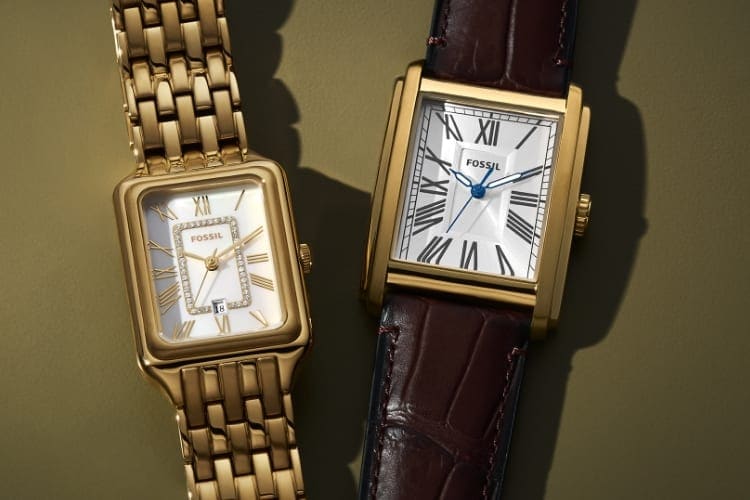 Zwei Uhren, die flach auf einem olivgrünen Hintergrund liegen. Beide haben weiße Zifferblätter und quadratische Gehäuse aus goldfarbenem Edelstahl; die linke Uhr hat ein siebengliedriges Band, die rechte Uhr ein braunes, geprägtes Lederband.