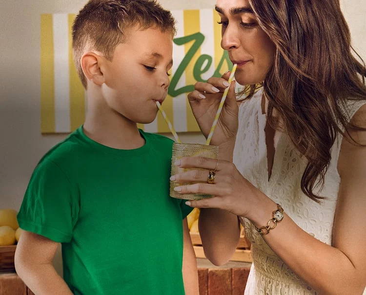 A mum and son sharing a glass of lemonade, sipping from yellow and white straws.