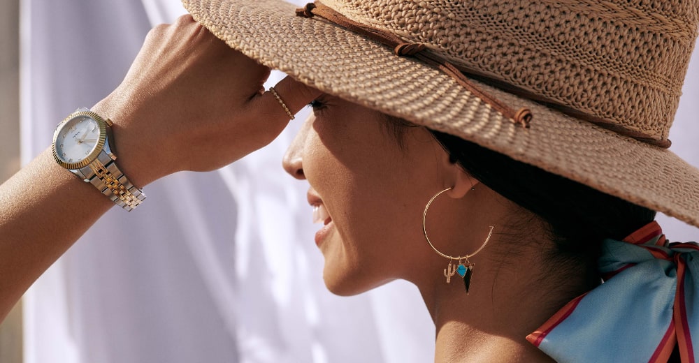 Eine Frau mit Hut trägt goldfarbene Creolen mit Charmanhängern.