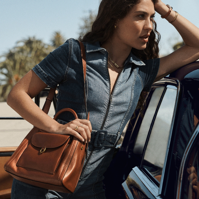 Una donna che indossa lo zaino Parker Mini in pelle marrone sulla spalla. Una donna che indossa lo zaino Parker Mini in pelle marrone a mano. Una donna che indossa lo zaino Parker Mini in pelle marrone sulla schiena.