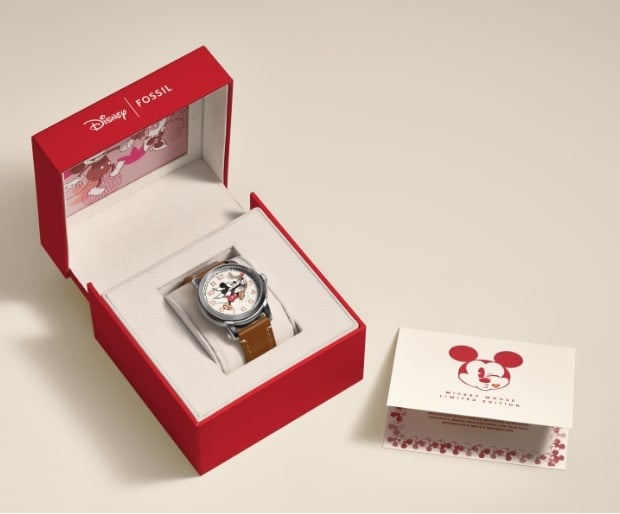 A GIF of the red Disney Mickey Mouse watch box that opens to reveal the exclusive Disney Mickey Mouse Cupid watch. A certificate of authenticity, featuring Mickey Mouse's face sits next to it.