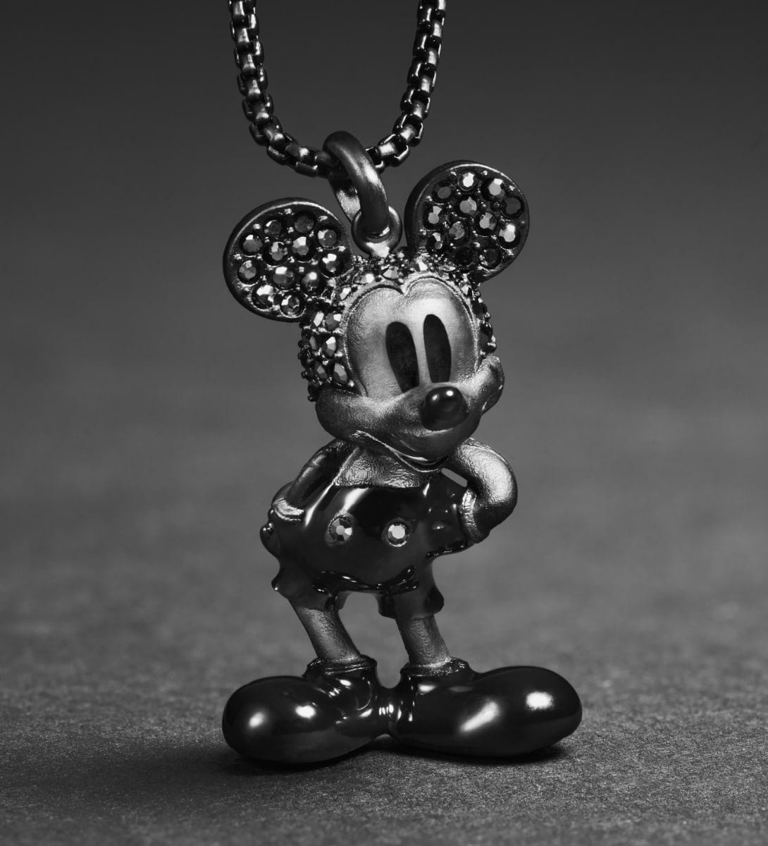 An animated GIF of two images. The first image features an all-black Mickey Mouse figurine pendant necklace studded with black hematite crystals. The second image showcases a gold-tone pendant of Minnie Mouse's profile, accented with crystals.