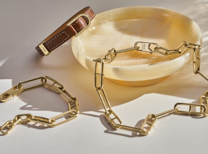 Bracciale, cinturino in pelle e collana Fossil Heritage D-Link su una ciotola di vetro.