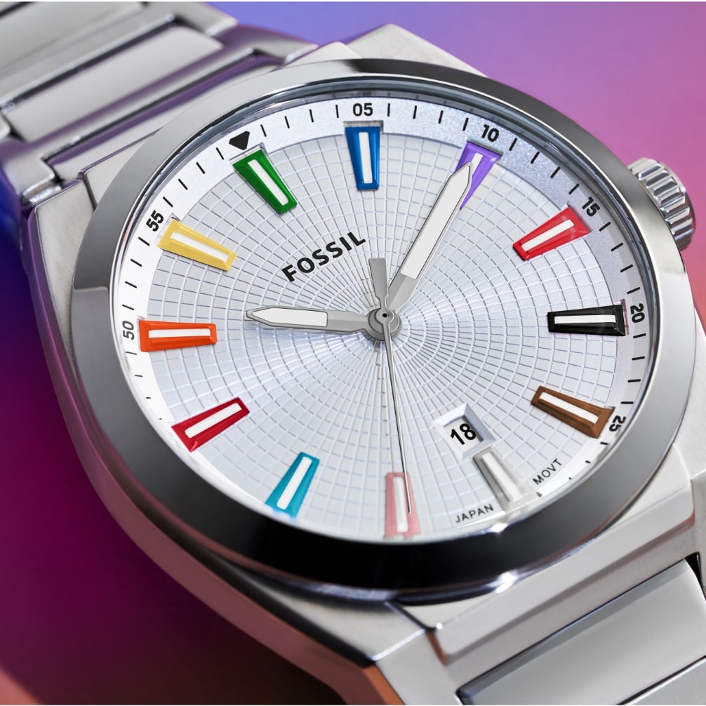 A silver unisex watch featuring a textured dial and rainbow indices that represent the colors of the Pride and Trans flags. The watch is set against a rainbow gradient background that transitions from purple to pink.