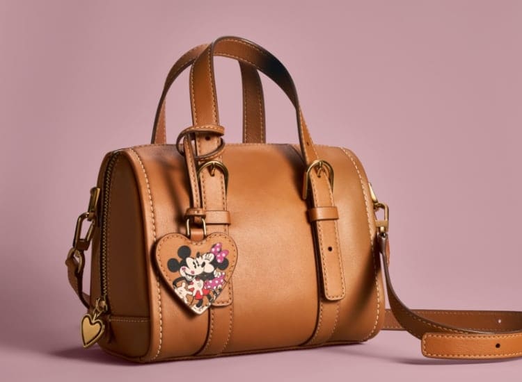 The brown leather Carlie mini satchel with a heart-shaped accent featuring an embossed graphic of Mickey Mouse and Minnie Mouse.