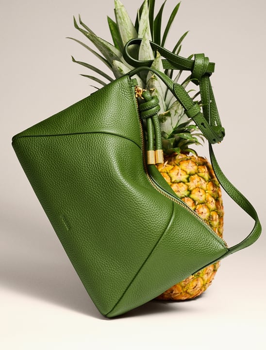 Image of a pineapple with a green leather Fossil bag sitting diagonally in front.