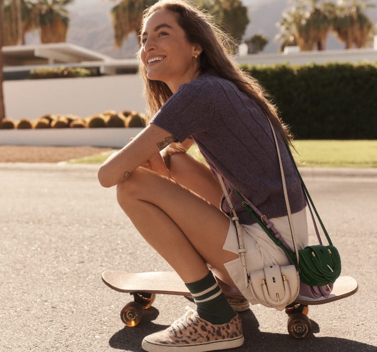 A gif of three micro bags in light purple, python-embossed green and ivory (clockwise from the top) and a woman sitting on a skateboard wearing the python-embossed green and ivory micro crossbody bags. 