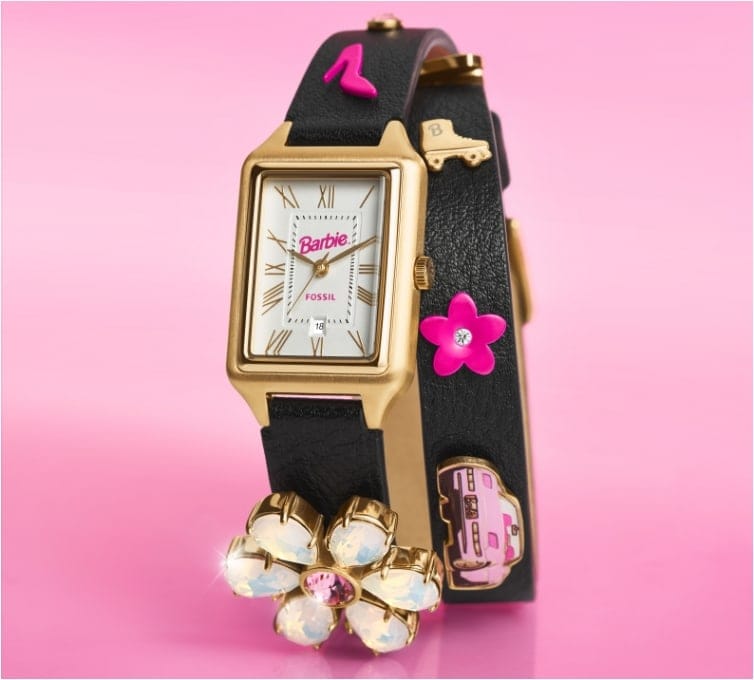 Un arrière-plan rose avec notre montre Raquel BarbieMC x Fossil en édition limitée, caractérisée par un bracelet noir avec icône comme une fleur de cristal, un patin à roulettes et une voiture rose.