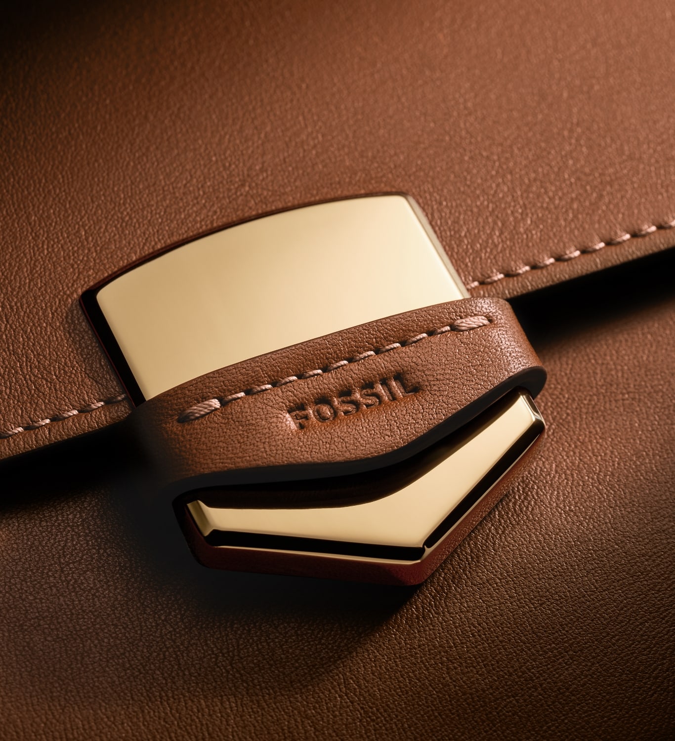 The gold-tone Fossil Crest on the brown leather Lennox bag, overlaid with a sketch of the Crest.
