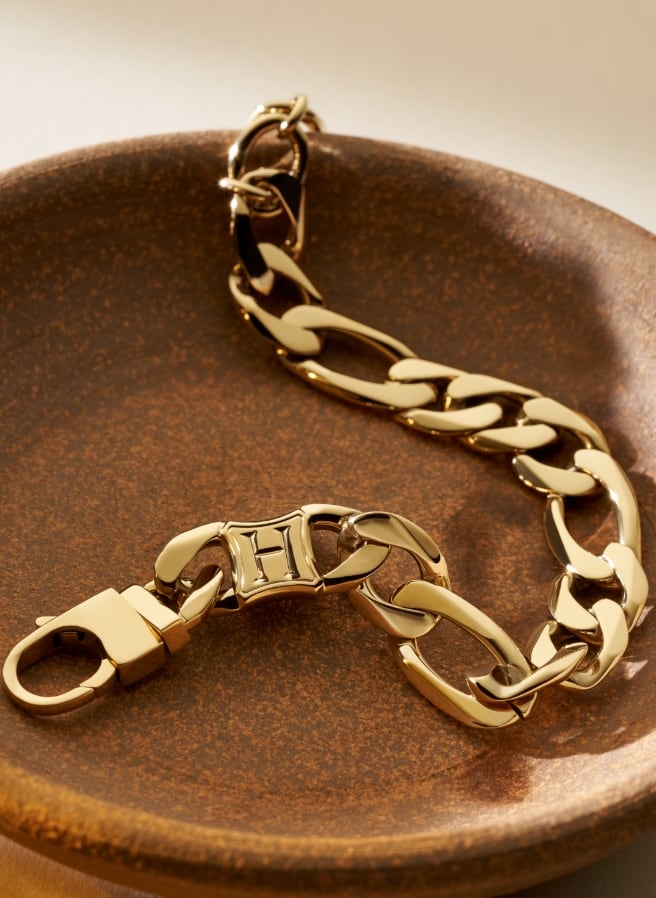 Pulsera de cadena en tono dorado con un eslabón en forma de “H”.