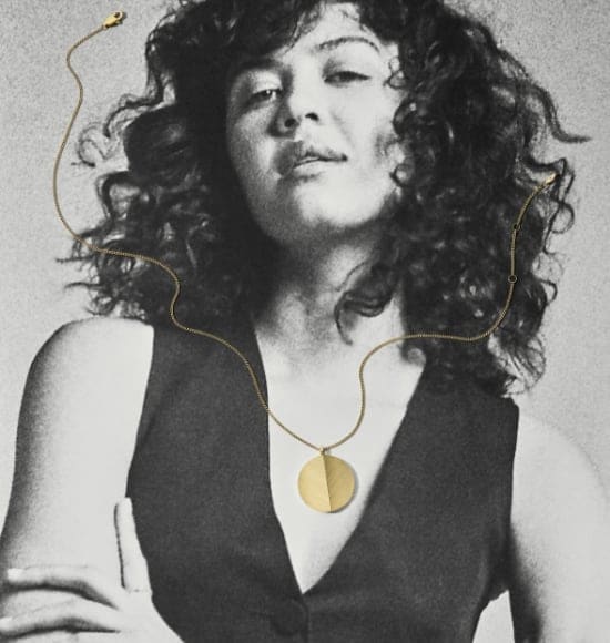A black and white photo of a woman with a gold-tone locket necklace draped over the image.
