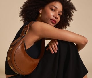 A woman in a black dress carrying the brown leather Harwell handbag.
