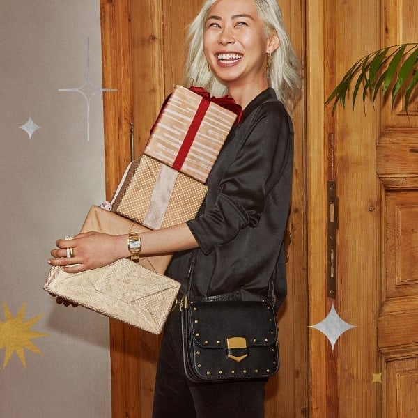 A woman smiling and holding a stack of presents wrapped in a red bow.