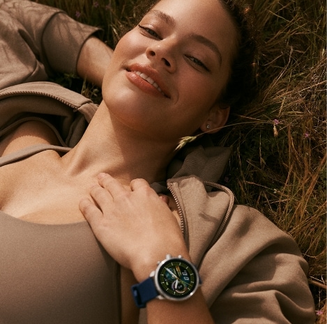 A woman lying in the grass while wearing a Gen 6 Wellness Edition smartwatch.