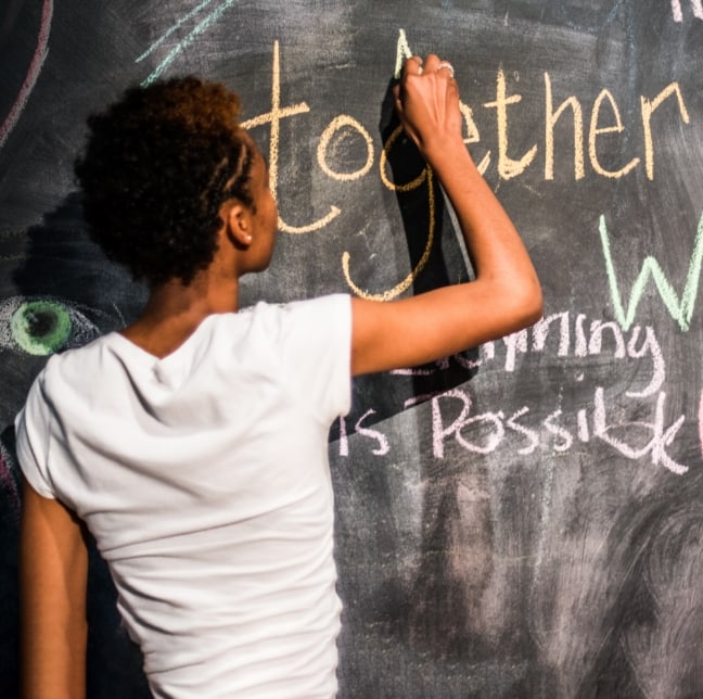 A young boy writing on a chalkboard.