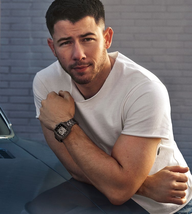 Nick Jonas leans against a vintage car wearing a white tee and the gunmetal Machine Luxe Automatic watch.