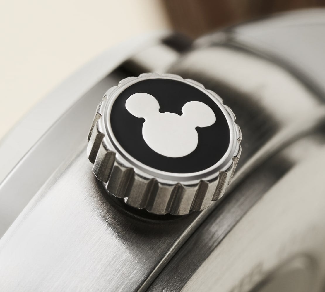 Une vue détaillée de la couronne de la montre avec la silhouette de Mickey argentée sur fond noir.