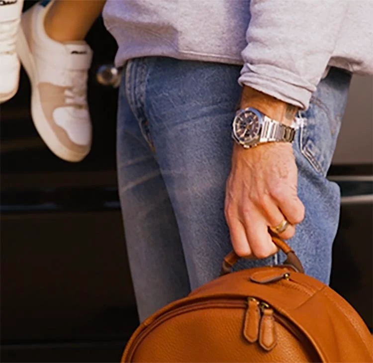 A dad casually dressed in jeans and the Everett chronograph watch, carrying his son and a leather bag.