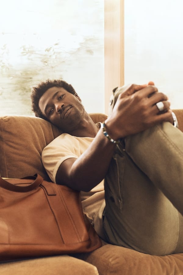A man sitting on a sofa and wearing Fossil jewelry from the summer collection.