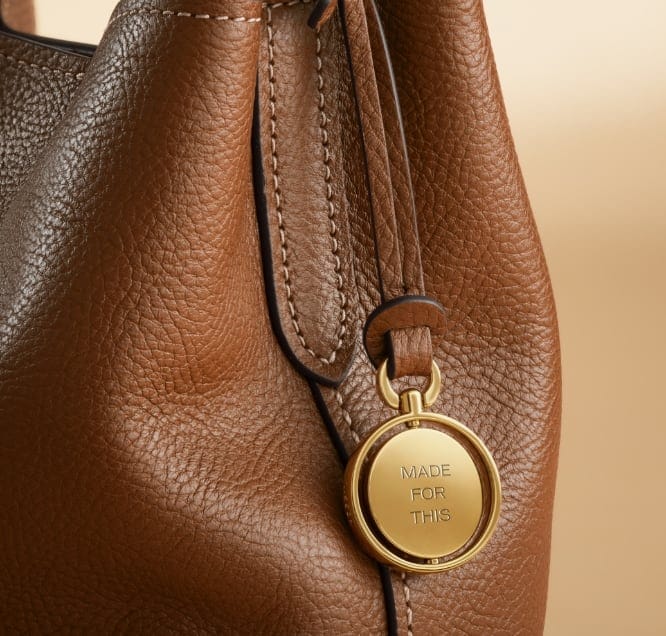 The Legacy Charm on the Jessie Bucket bag engraved with ABC in a script font.