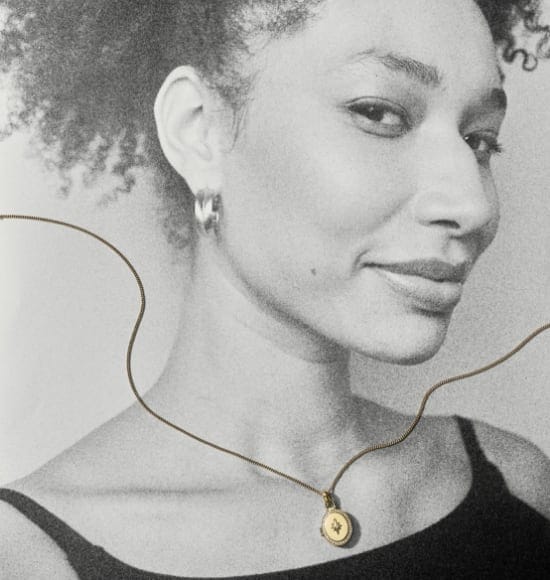 A black-and-white photo of a woman with a gold-tone locket necklace and a silver-tone earring draped over the image.