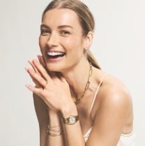 Une femme souriante portant un bijou Fossil doré.